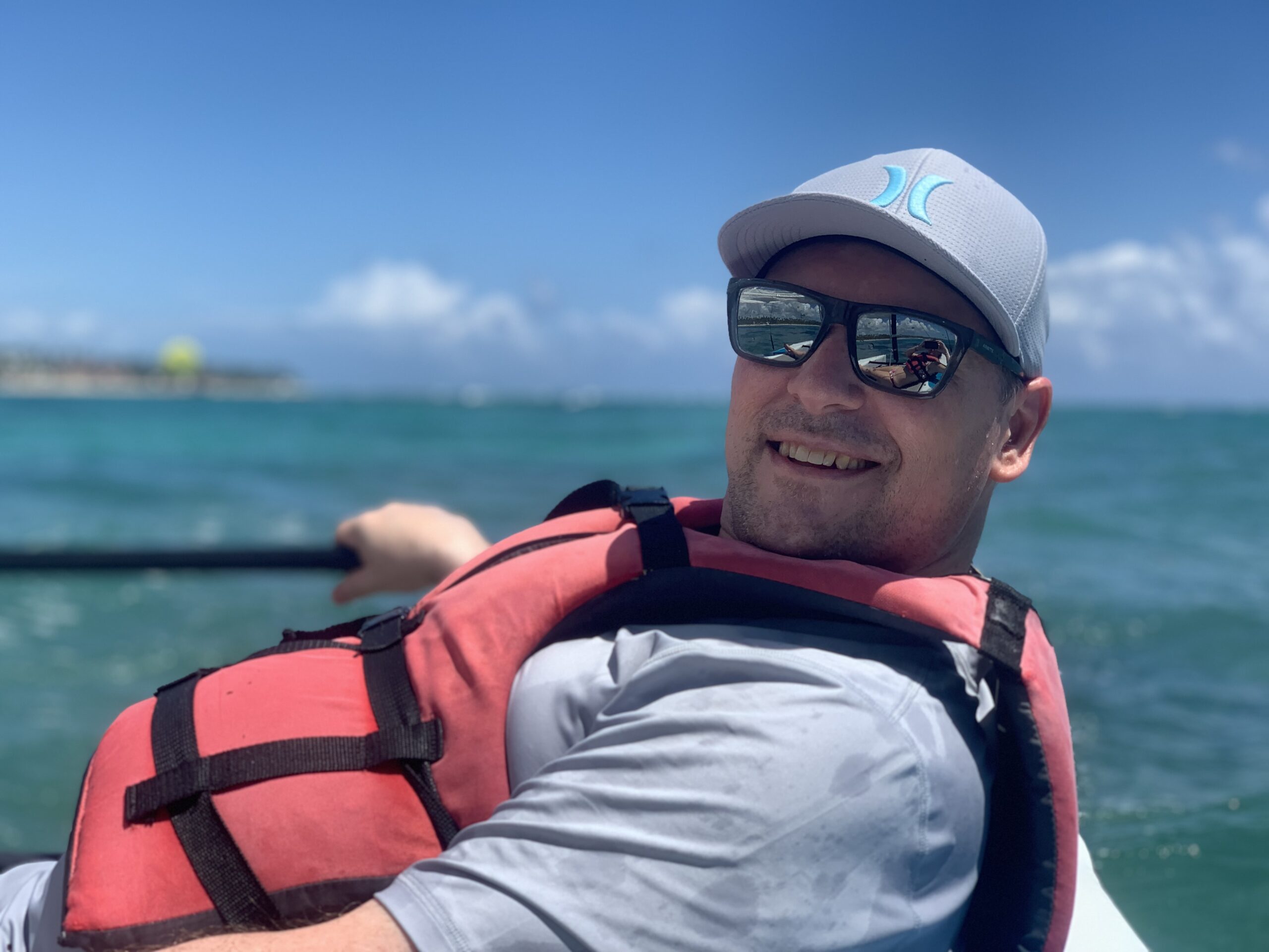 Photo of Jack in a boat wearing a baseball hat, sunglasses, and a life preserver