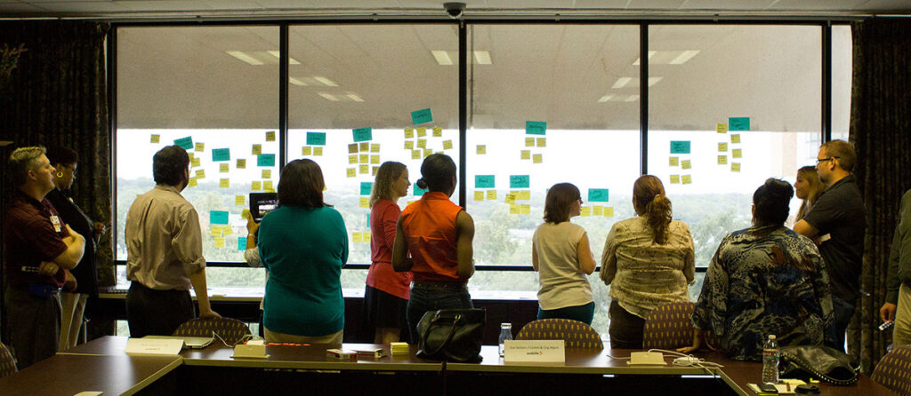 People standing in front of window with sticky notes, doing a KJ session