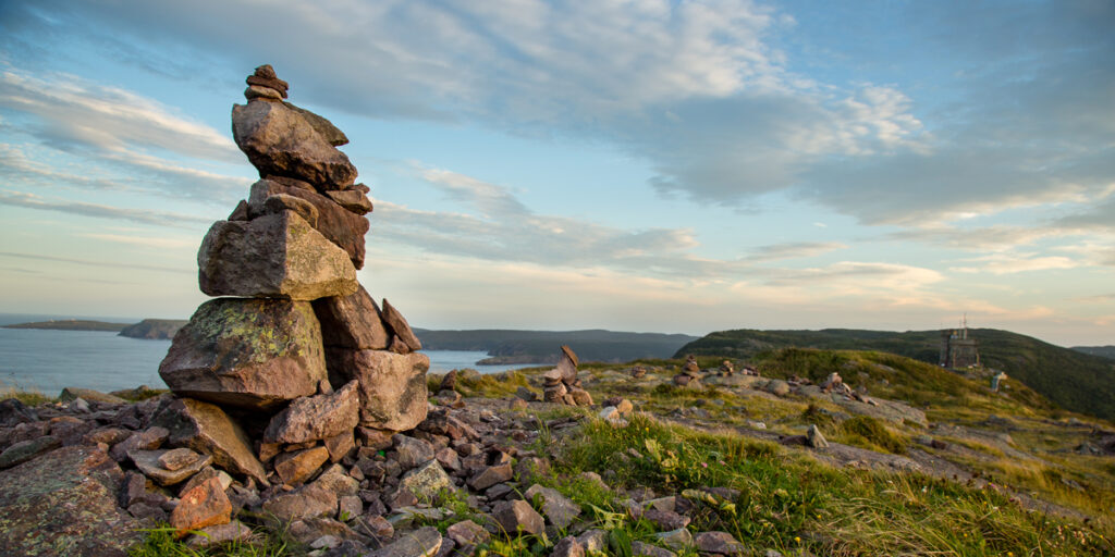 photograph of a stone cairn on a mountaintop overlooking a rugged coastline below.