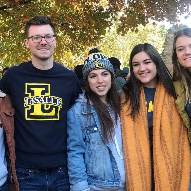 Five La Salle students in cool weather clothing and standing under a tree smile at the camera.