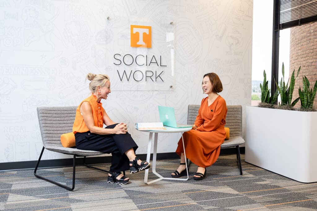 Two women sit talking in a lobby on the College of Social Work campus